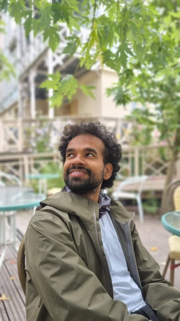Avi Pandit outdoors, smiling, with green foliage